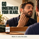 Man working Samson's Beard Oil into the skin under his beard in front of a mirror