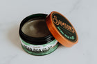 4 oz container of Dead Sea Clay with cap removed and leaning against the side, revealing the styling clay inside.