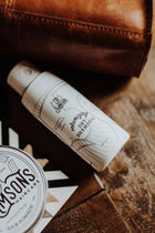 1.4 oz Volumizing Matte Powder bottle lying on its side next to hair pomade, both on a wooden table with a brown bag, in a casual setting.