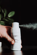 Hand squeezing a 1.4 oz Volumizing Matte Powder bottle, demonstrating the spray application.