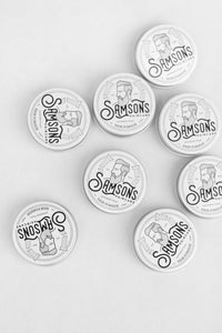 Overhead view of 1 oz hair pomades with the old logo spread out on white surface.